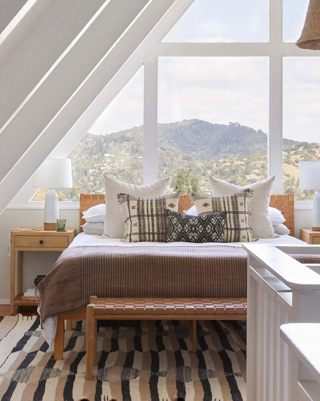 Beige woven leather bench with teak frame and mid-century turned legs in a bright bedroom with a view