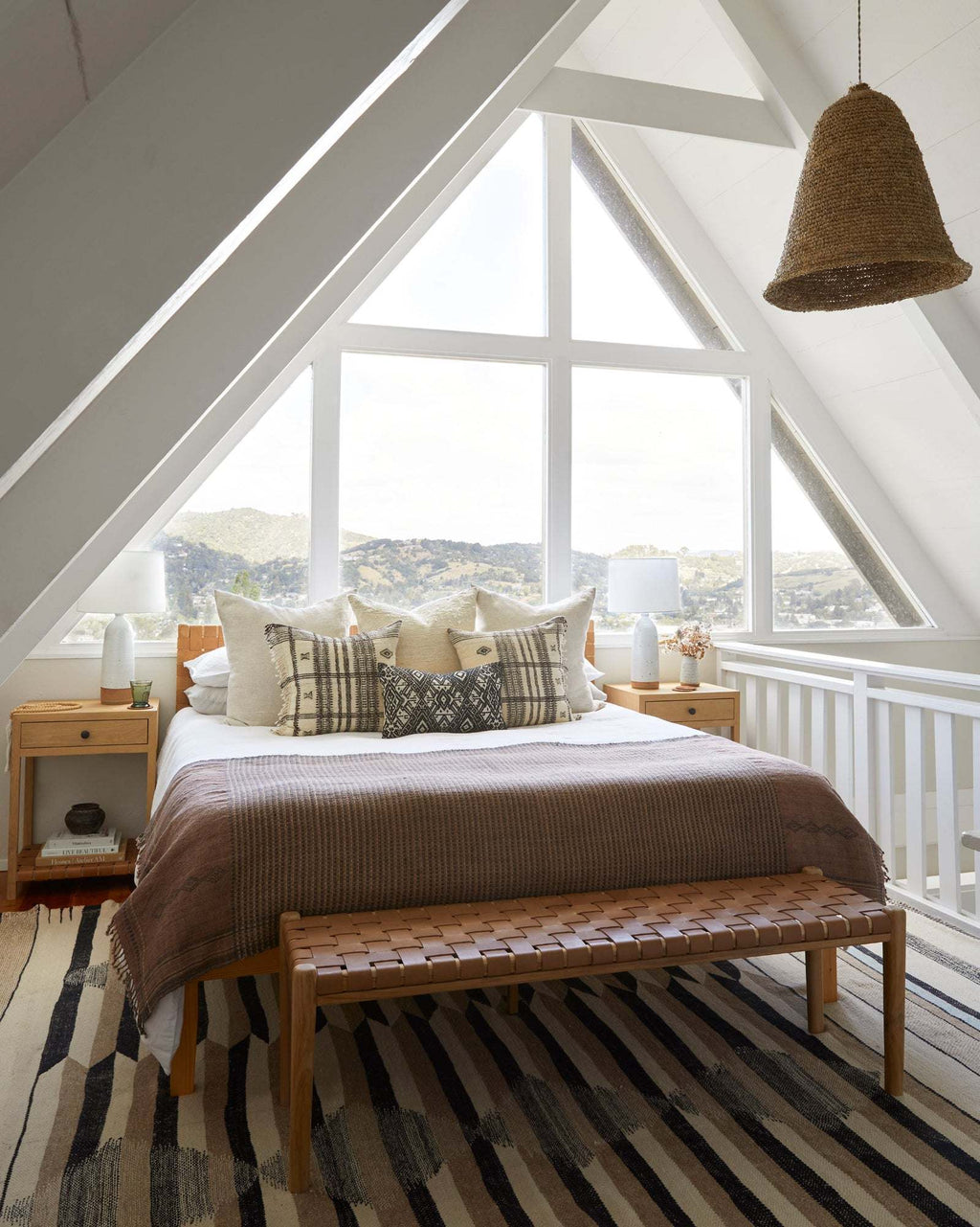 Beige woven leather bench with teak frame and mid-century turned legs in A-frame bedroom with tall windows