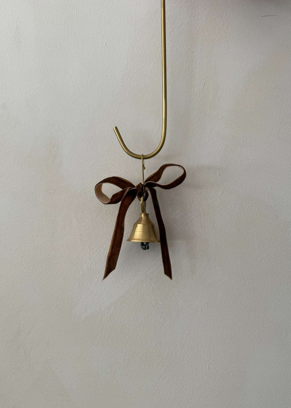 Brass bell ornament with cinnamon velvet ribbon hanging on a Christmas tree branch