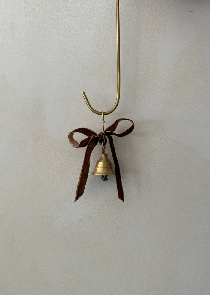Small brass bell ornament with a brown ribbon on a white background