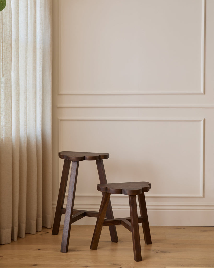 Wooden cloud shaped stools against a neutral wall with a curtain
