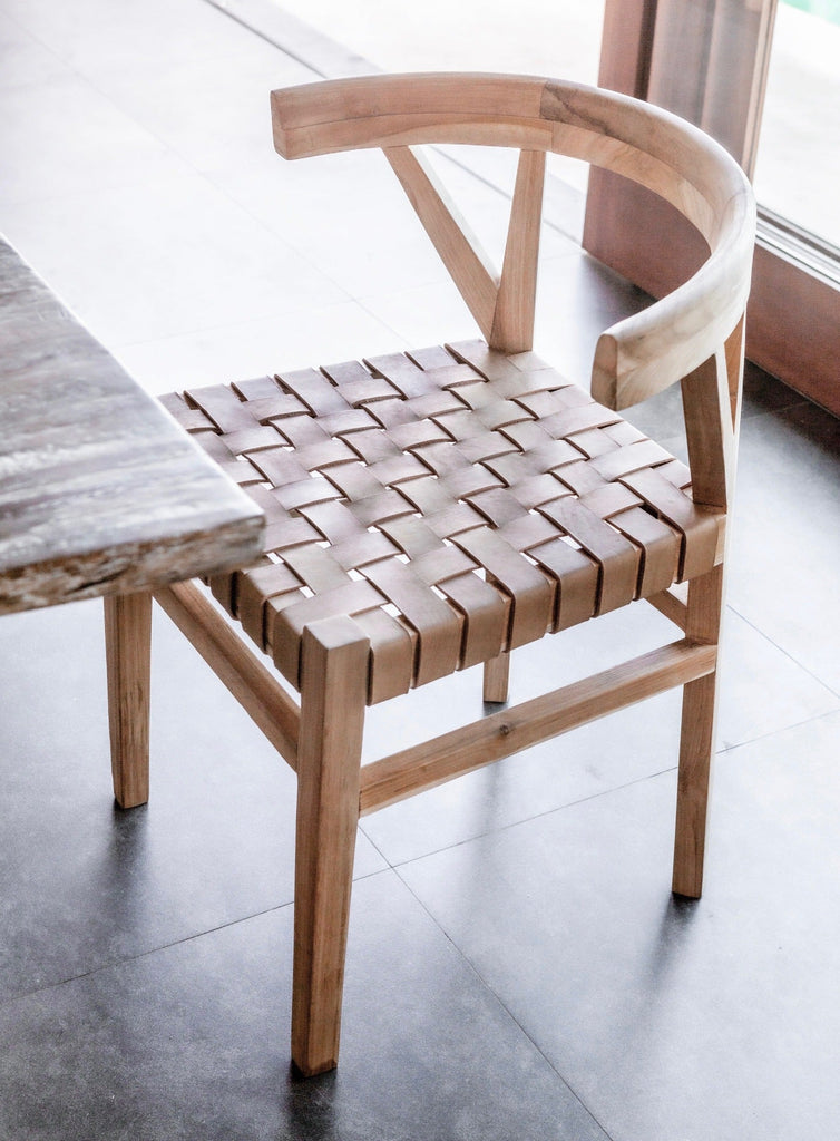 One curved wood and woven beige leather dining chair inspired by the wishbone Chair at the kitchen table. Handcrafted in Bali with Teak wood and vegetable-tanned leather imported from Java. - Saffron and Poe