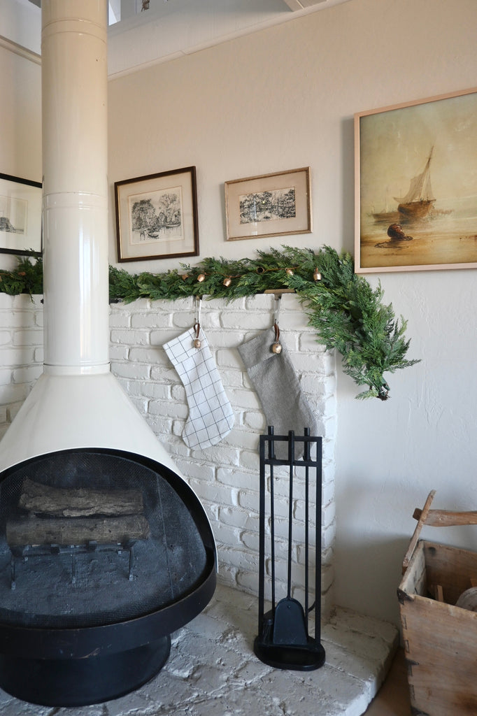 Nestled corner of a room with a white brick fireplace, stockings hanging, and decorative greenery.