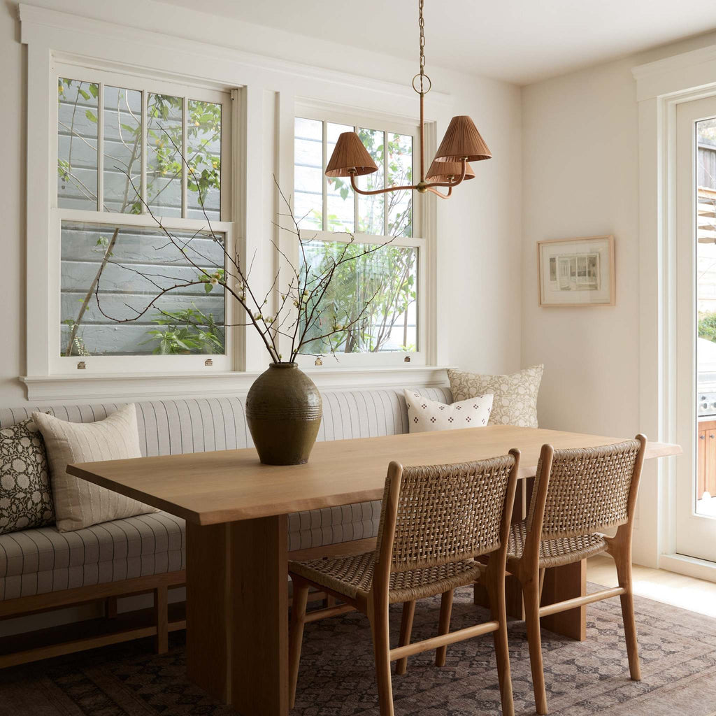 Delphine Chandelier in a breakfast nook setting over dining table with vintage vessel with branches and an upholstered banquette. 