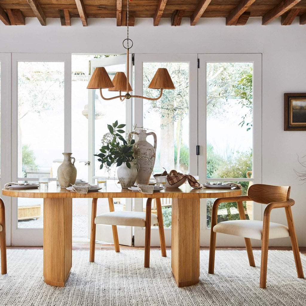 Dining room with wooden table and chairs, large windows, a Delphine chandelier, and decorative items.