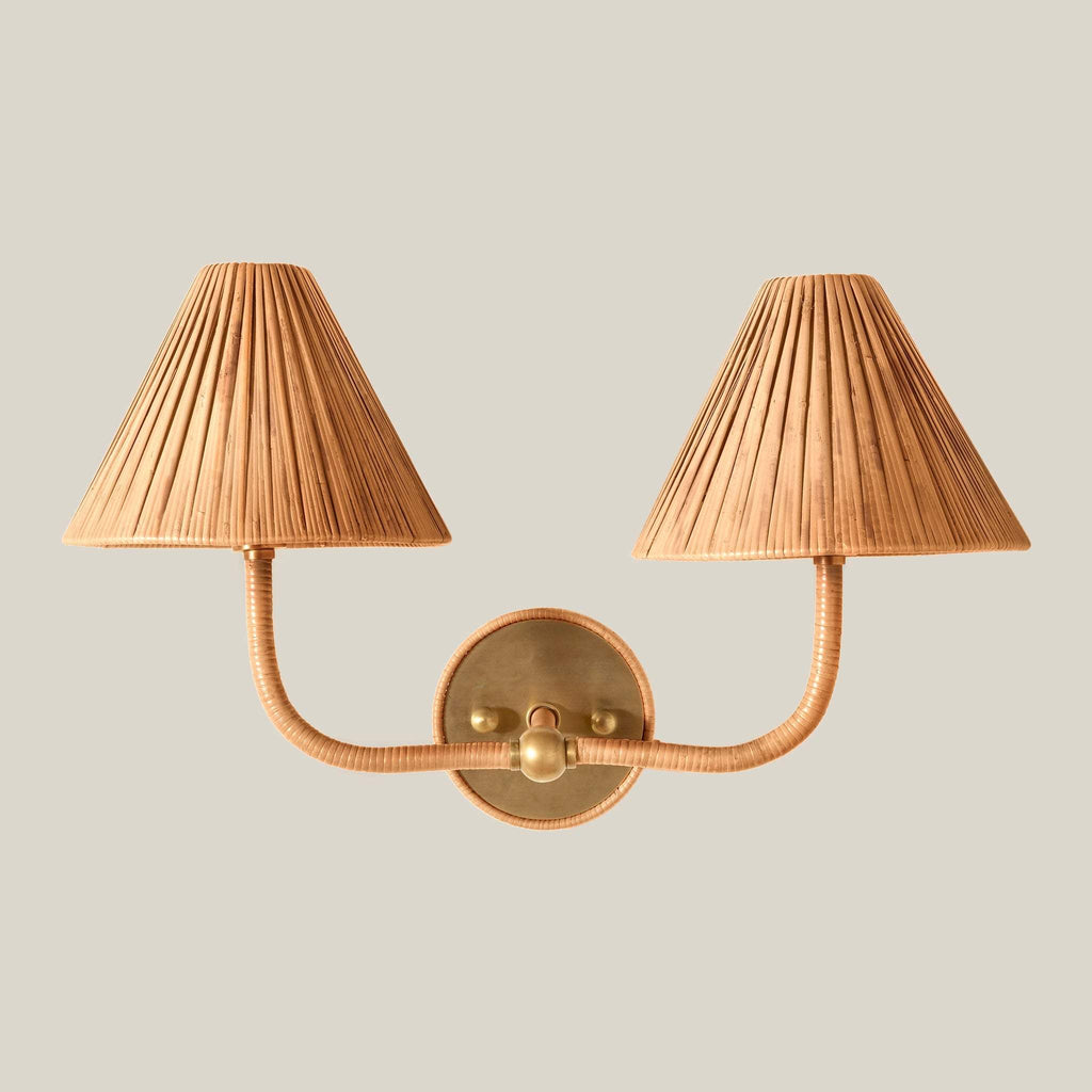 A two-light Delphine wall sconce with pleated beige fabric shades and a warm brass metal frame, shown against a solid light gray background.