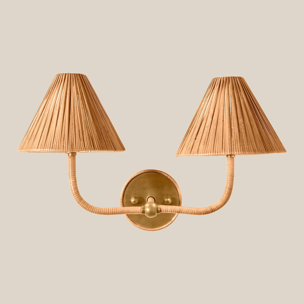 A two-light Delphine wall sconce with pleated beige fabric shades and a polished brass wall mount and curved arms, shown against a solid light beige background.