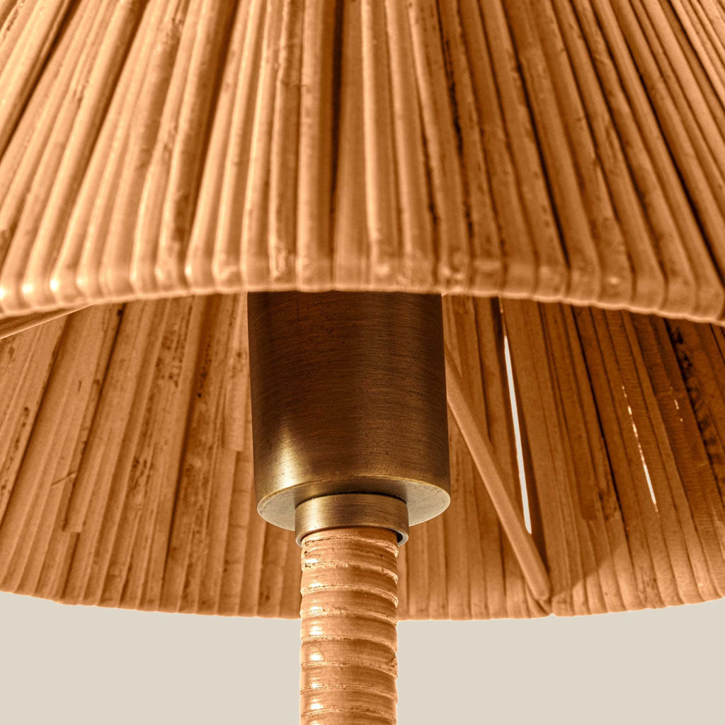 Close-up detail of a natural rattan Delphine sconce lampshade with a warm brass metal neck and a textured woven stem, shown against a light neutral background.