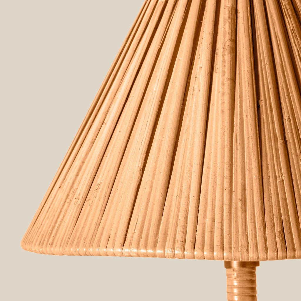 Close-up of a pleated lampshade made of natural woven material, showing vertical slats and a warm tan color, with part of the matching ribbed stem visible at the bottom against a light neutral background.