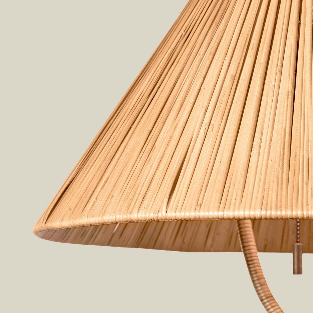 Close-up of a woven natural rattan Delphine floor lampshade with a curved underside and a hanging pull chain, shown against a plain light beige background.