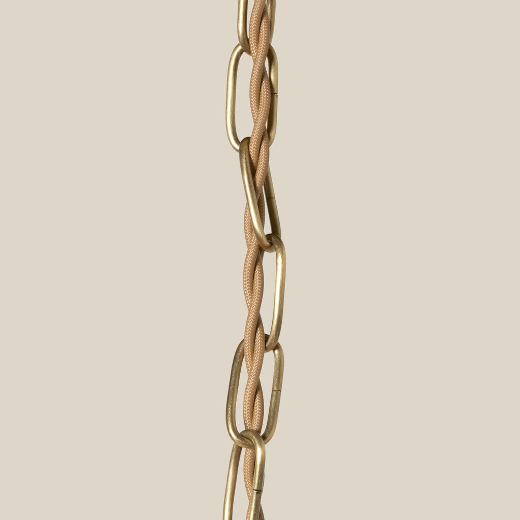 A close-up of a gold-toned chain with elongated oval links and a braided beige cord running through the center, set against a solid light beige background.