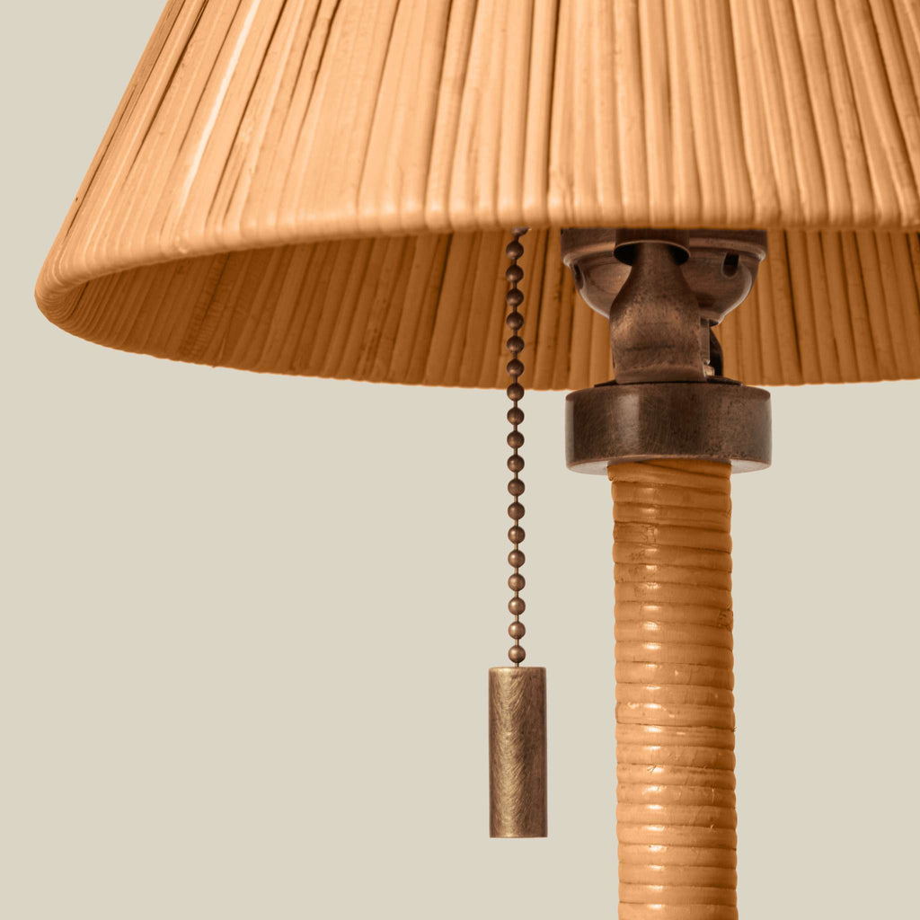 Close-up of a Delphine Mini table lamp with a pleated beige shade, a textured beige column, and a dark metal pull chain with a cylindrical weight, shown against a light gray background.