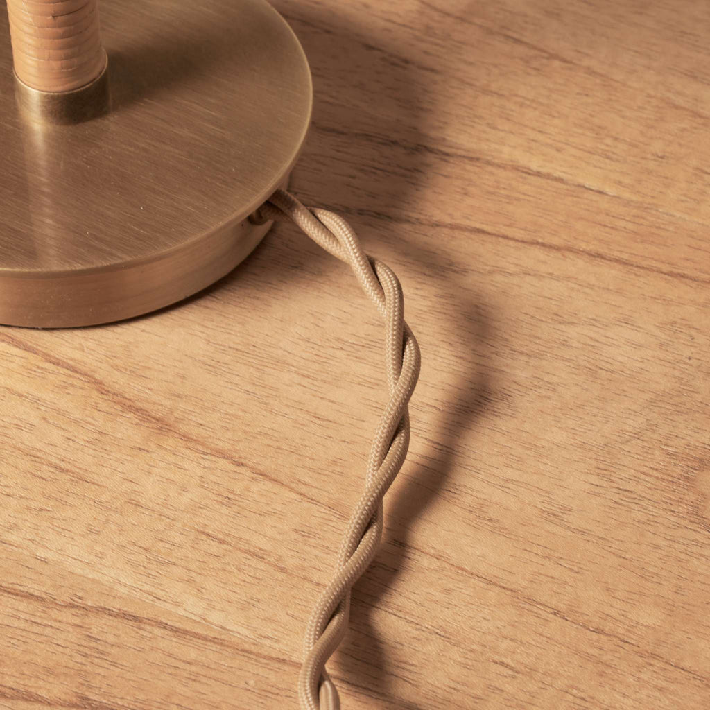 Close-up of a bronze lamp base on a wooden surface with a braided cable.
