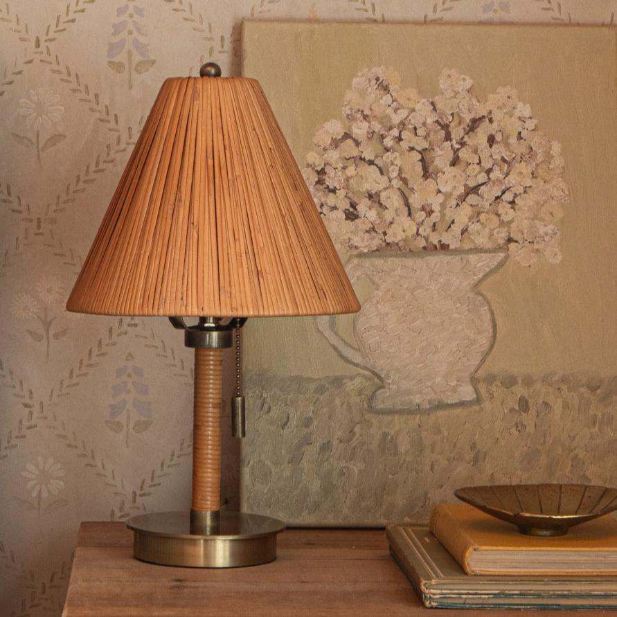 Delphine Mini Table lamp with pleated shade on a wooden surface, floral painting in the background