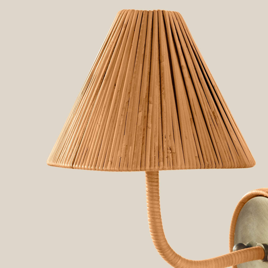 A close-up of a Delphine Sconce in a warm natural tan color, attached to a matching curved arm with a visible metal wall mount against a plain light beige background.