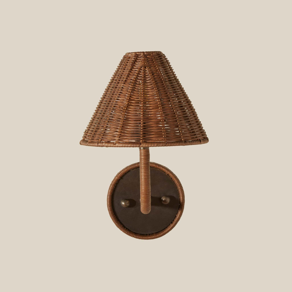 Delphine wicker wall sconce with a conical woven brown lampshade and a round pewter backplate, shown against a solid light beige background.