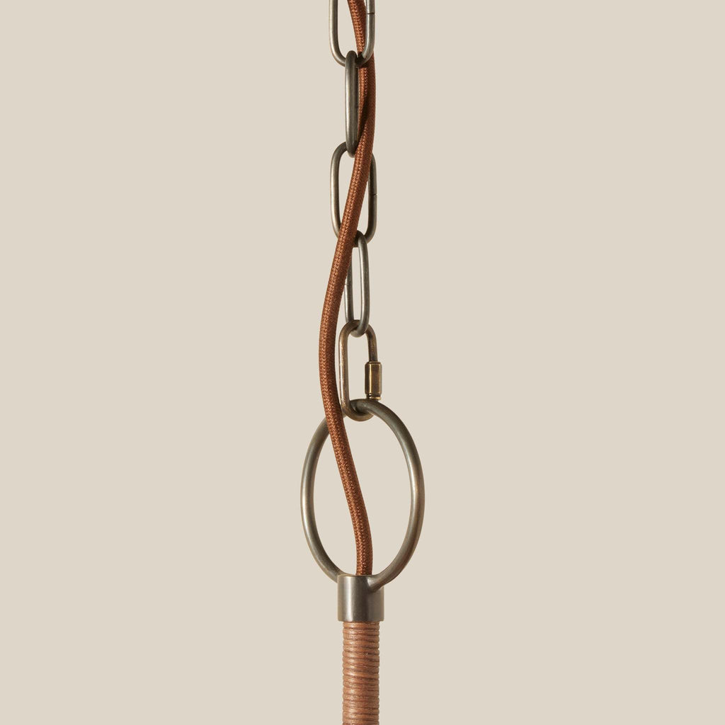 Close-up of Delphine Chandelier hanging chain with a central brown leather or fabric loop, pewter metal ring hardware, and a wrapped cord section against a plain warm beige background.