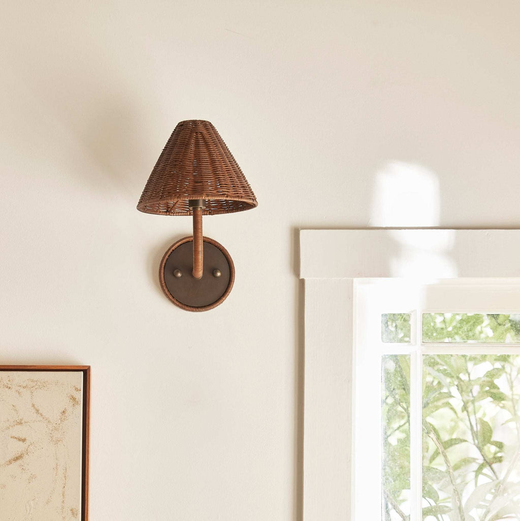 Delphine wicker wall sconce on a neutral wall with a window in the background.