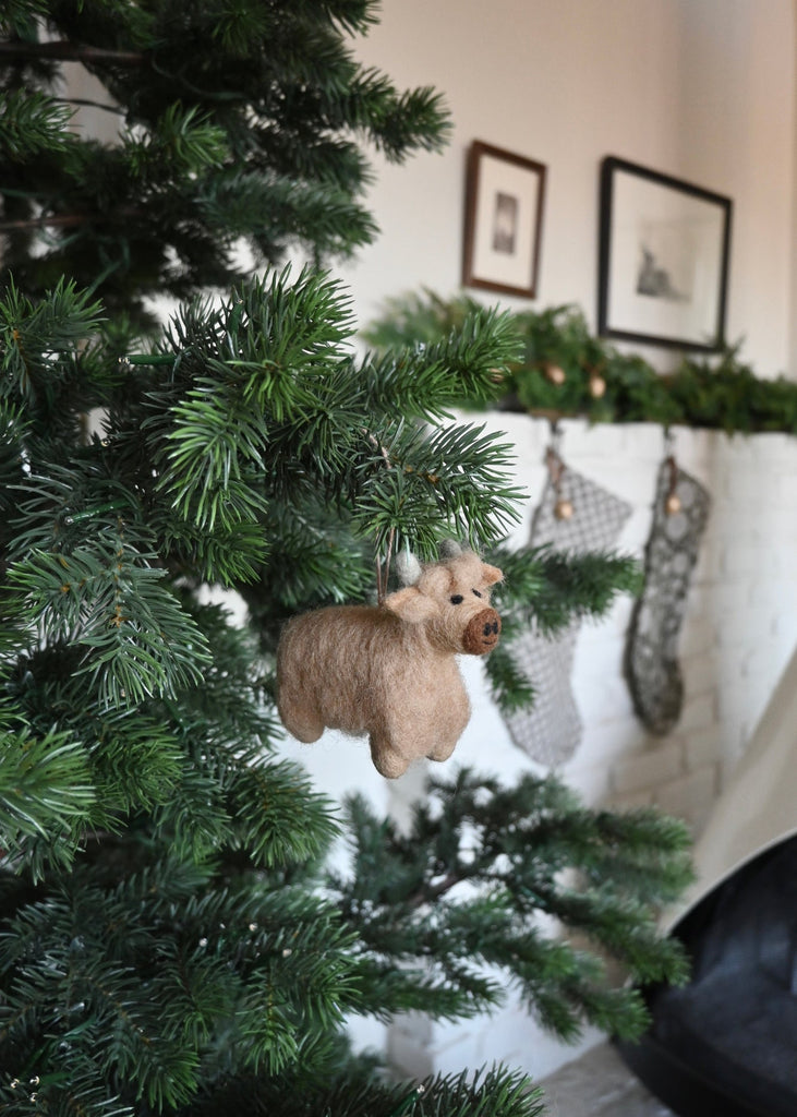 Small brown felt shetland cow ornament hanging on a Christmas Tree. Saffron + Poe