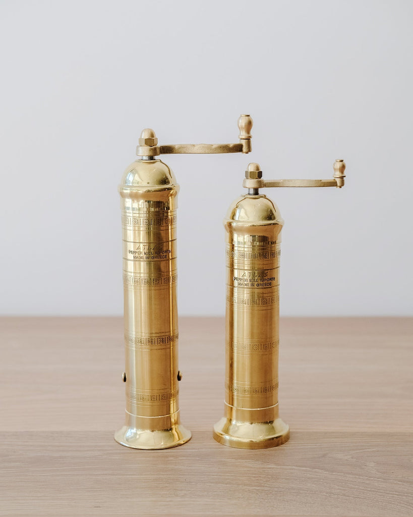 Front view of Atlas Brass Salt and Pepper Grinders - 8", 9" on an oak table against a white wall