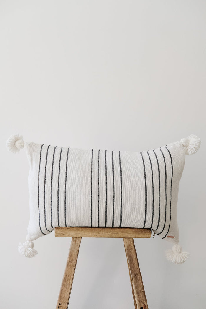Front view of No. 42 - Moroccan Pom Pom Striped Pillow - Black on a Chinese Stool against a white wall. - Saffron and Poe