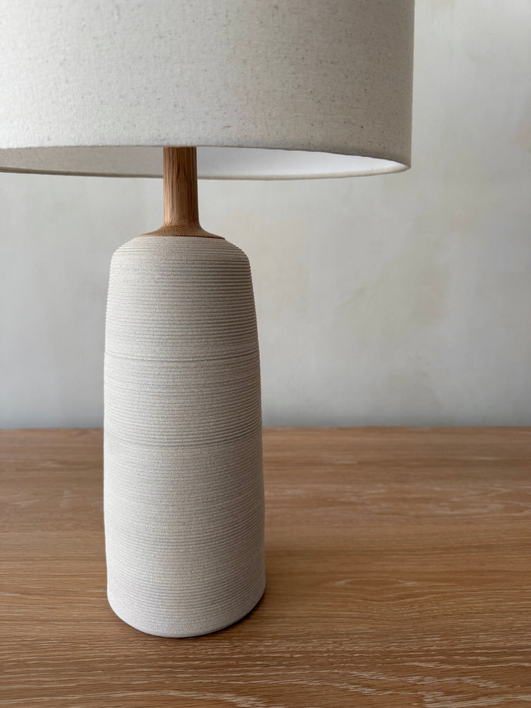 Ostuni Ceramic Table Lamp in Ivory with oatmeal linen shade close up shot on white oak table. - Saffron + Poe