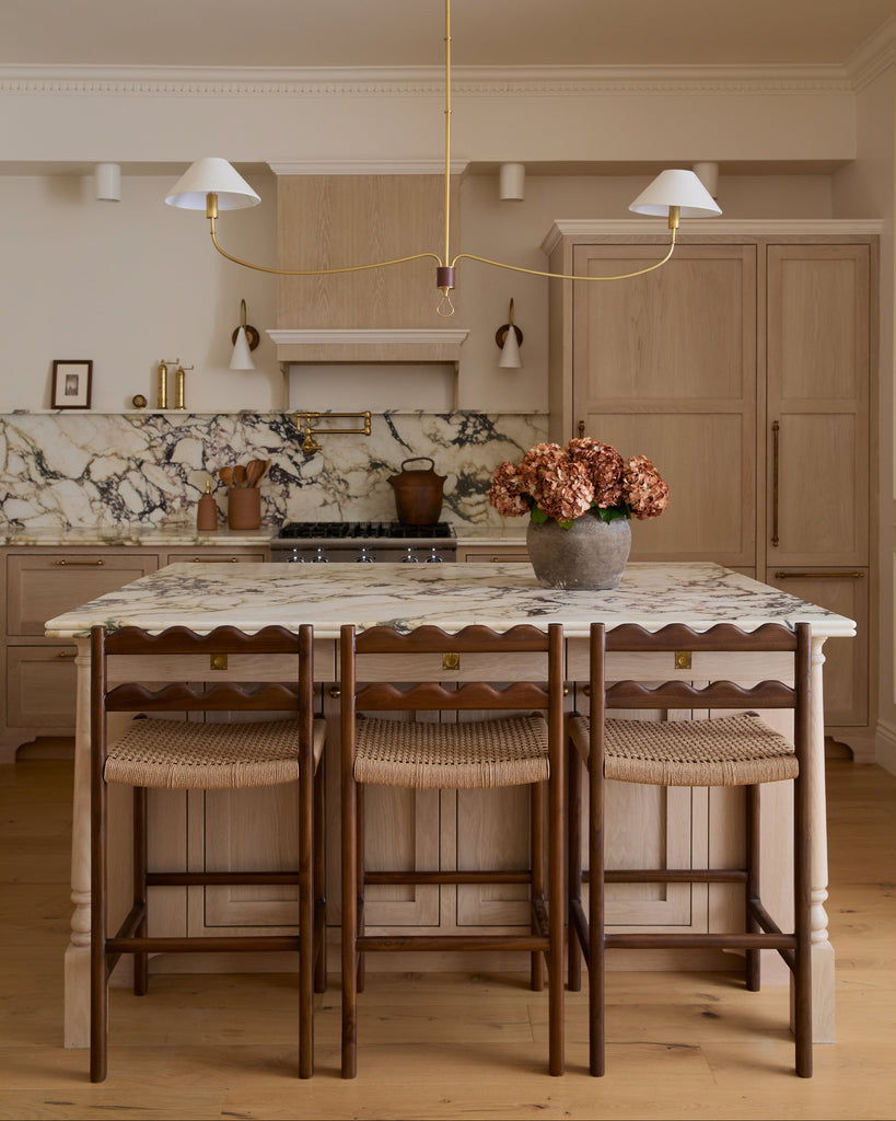 Ionian scalloped counter stool with woven seat in a white oak kitchen with marble counters. Saffron and Poe