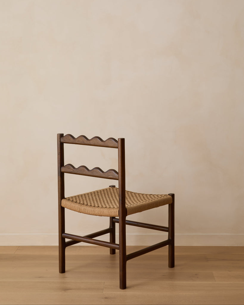 Ionian scalloped dining chair with woven seat on white oak flooring against a beige wall. Saffron and Poe