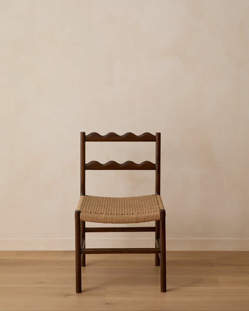 Ionian scalloped dining chair with woven seat on white oak flooring against a beige wall. Saffron and Poe