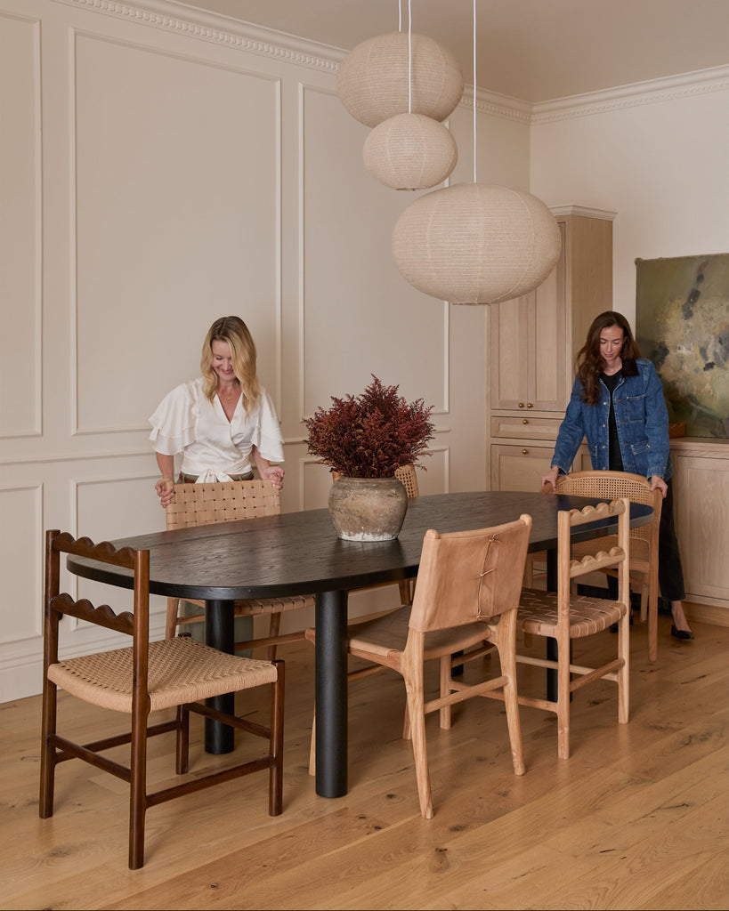 Ionian scalloped dining chair with woven seat in dining room with a black table, white oak flooring and paneled walls with people styling. Saffron and Poe