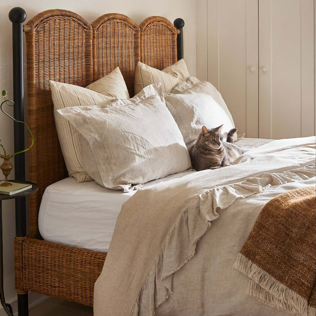 Rattan and iron Lacoste Queen Bed with a cat lying on a bed with natural and white bedding. 