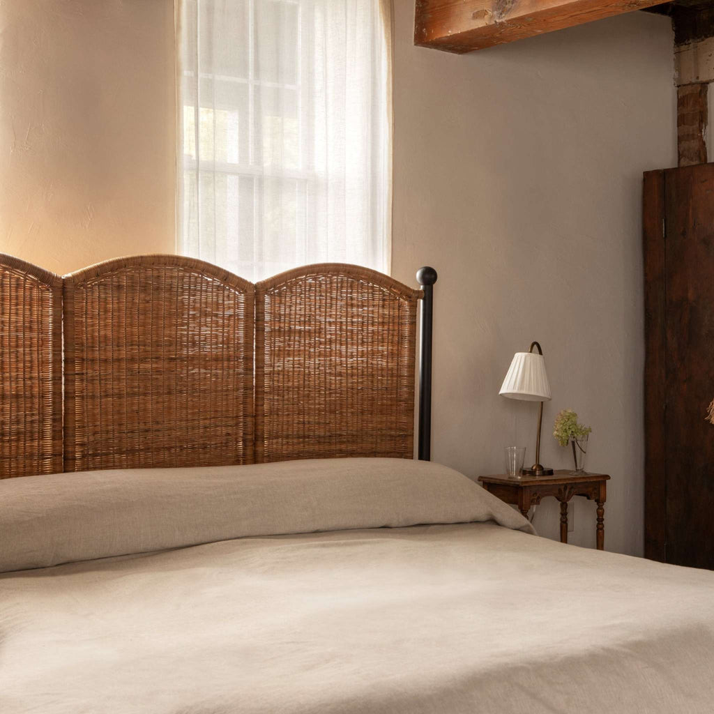 Bedroom with woven rattan and iron Lacoste bedframe and a lamp on a nightstand.