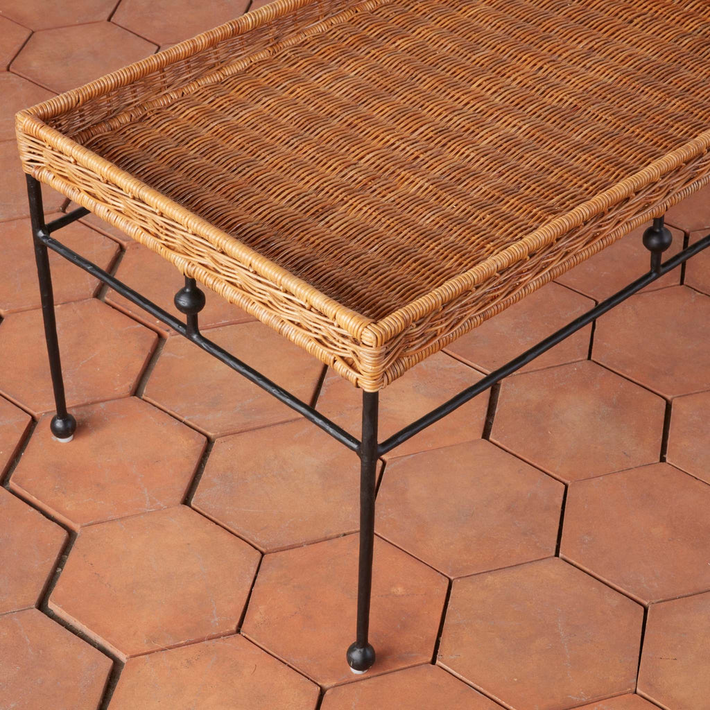 Lacoste rattan coffee table detail with black metal legs on a terracotta tiled floor.