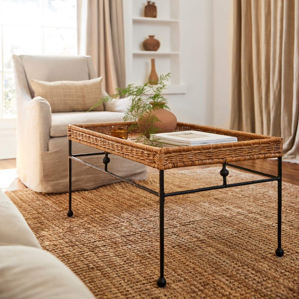 Lacoste indoor-outdoor rattan coffee table in a living room with a beige linen armchair and decorative items.