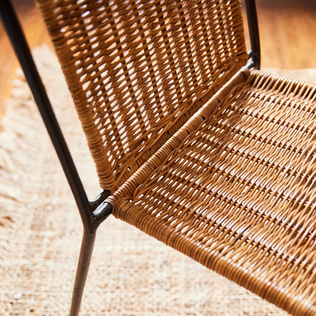 Close-up of rattan Lacoste Dining Chair with metal frame on a textured rug.