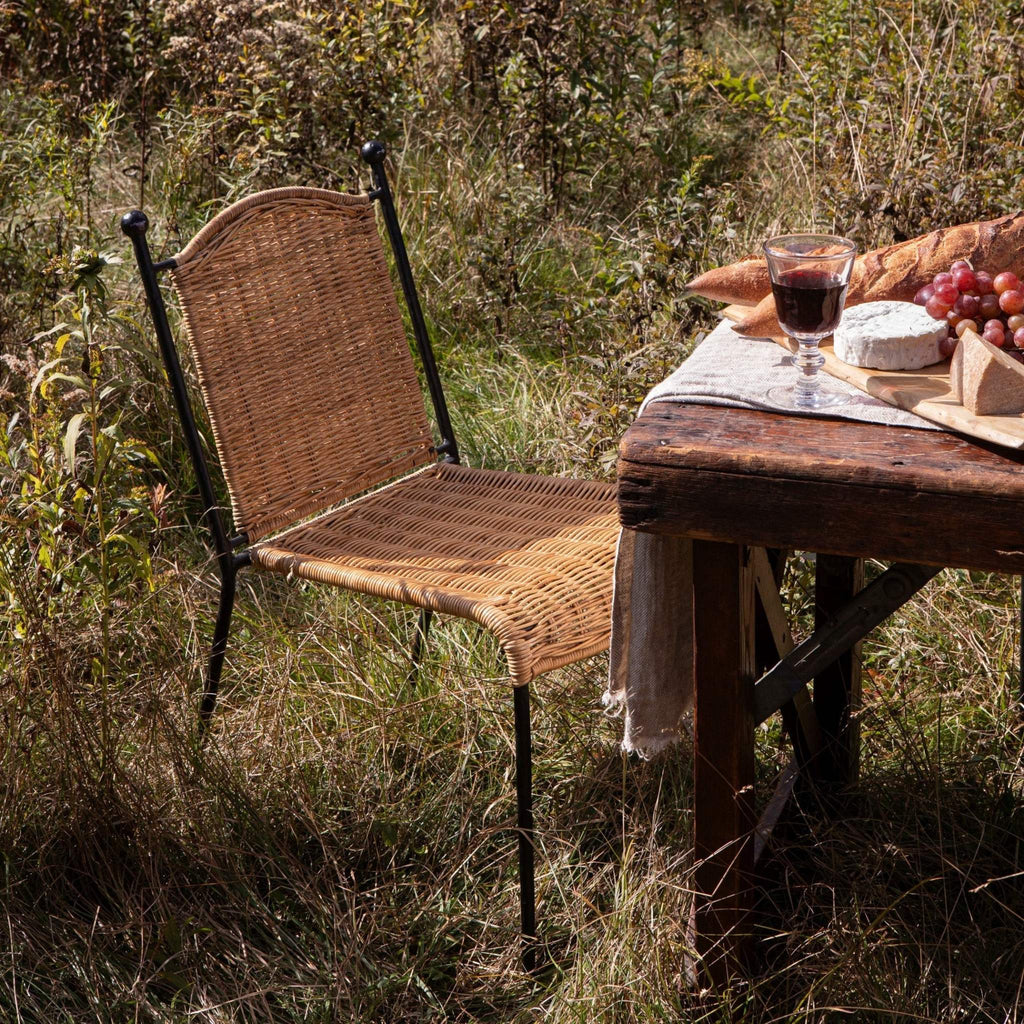 Lacoste Indoor-Outdoor dining chair and wooden table with food and wine in a natural outdoor meadow setting. 