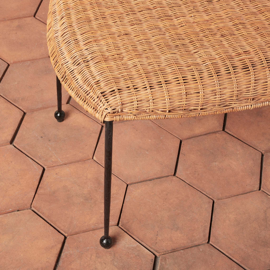 Detail of Lacoste indoor outdoor woven rattan bench with black iron legs against terracotta tile floor