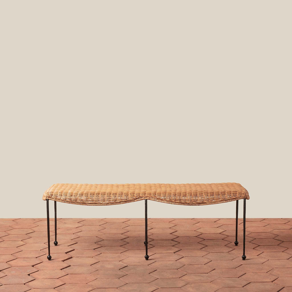 Lacoste woven rattan bench on a terracotta tile floor with a beige wall background