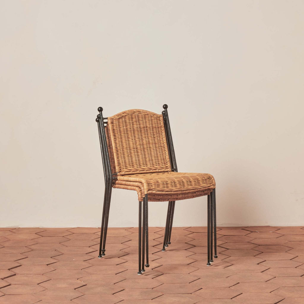 Three stacked Lacoste Rattan Indoor-Outdoor Dining Chairs with black metal frame on a tile floor against a beige wall