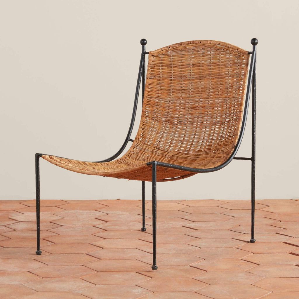 Woven rattan Lacoste Lounge Chair with an iron metal frame on a tile floor.