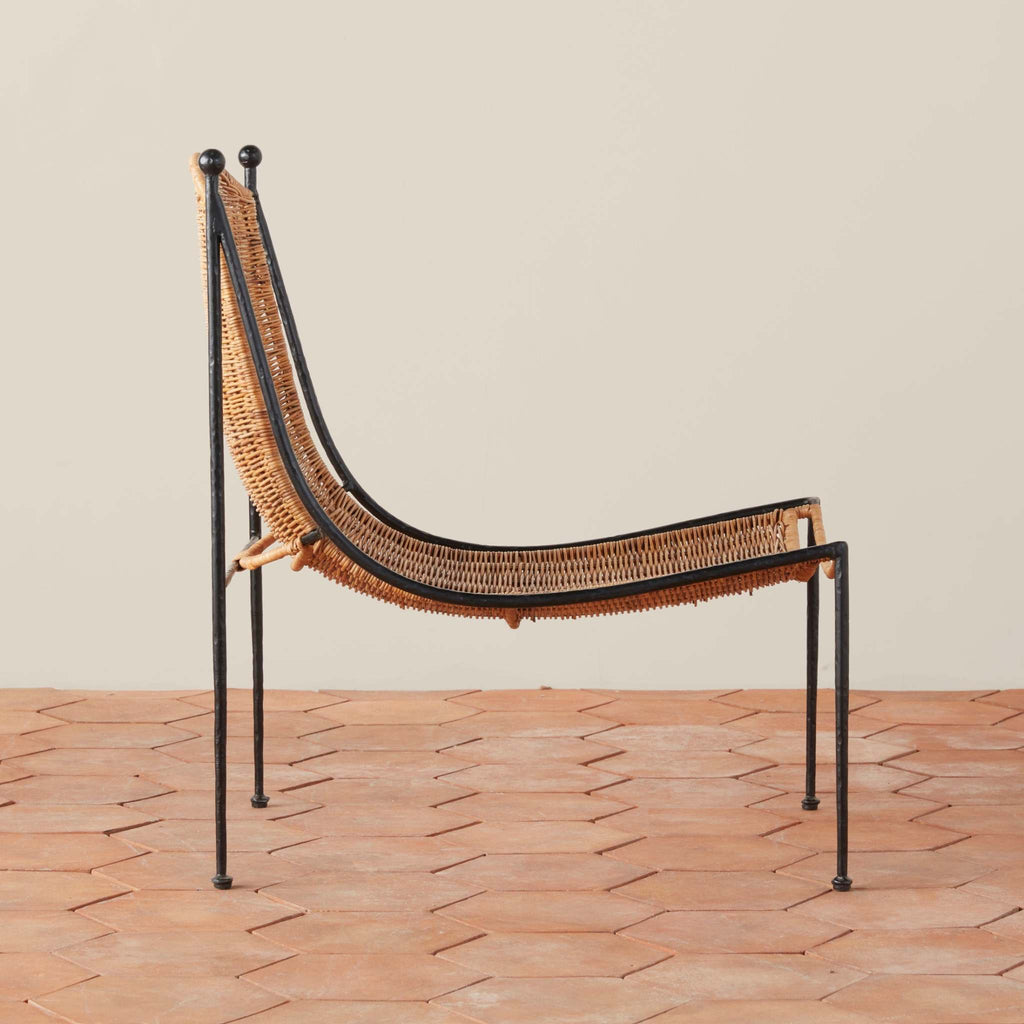 Side view of Lacoste wicker lounge chair with black metal iron frame on a terracotta tile floor.