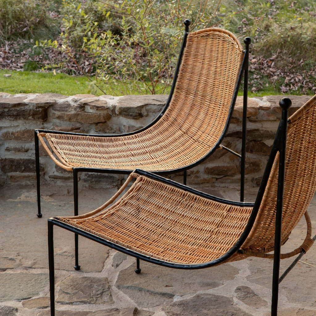Two wicker Lacoste lounge chairs on a stone patio with a garden background