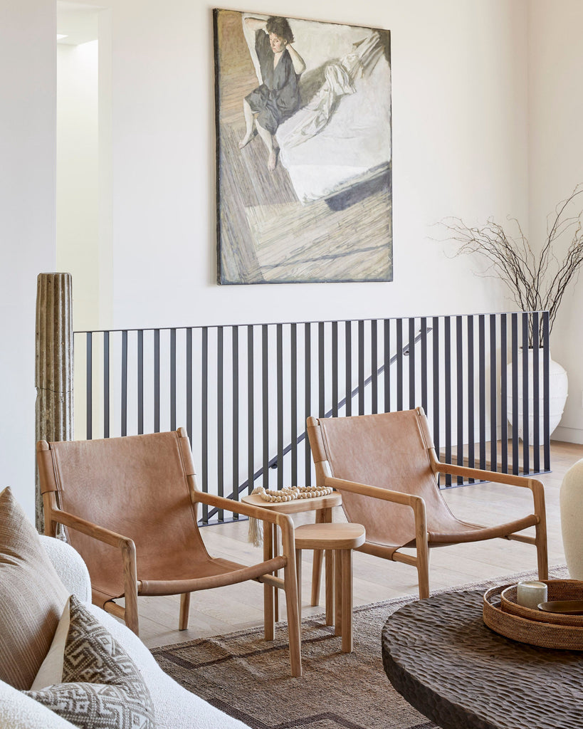 Living room with two sling lounge leather chairs, a small table, and a painting on the wall.