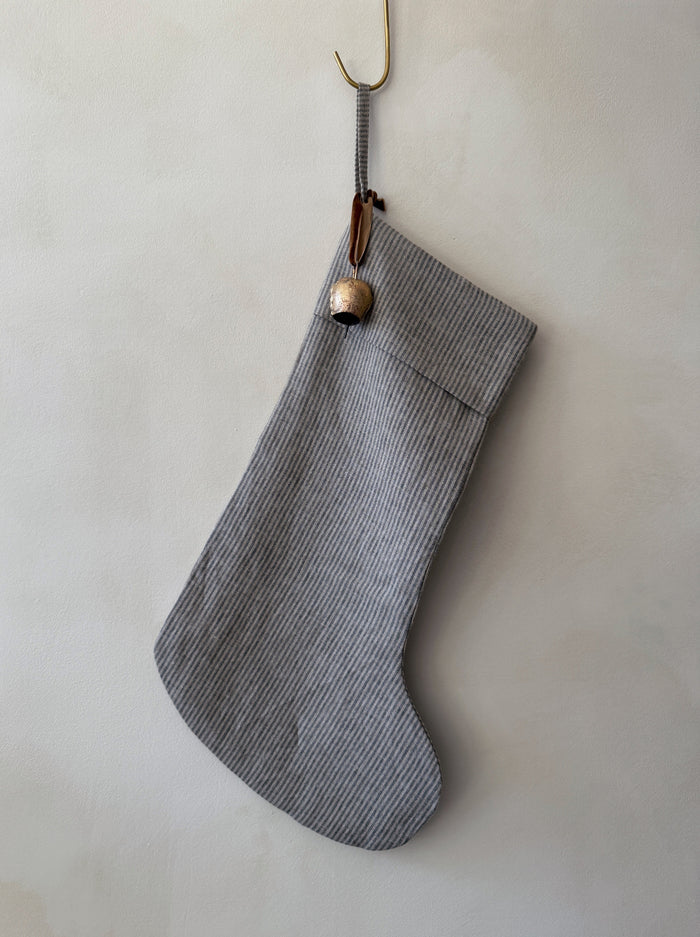 Gray striped linen Christmas stocking with an antique bell on a white background - Saffron + Poe