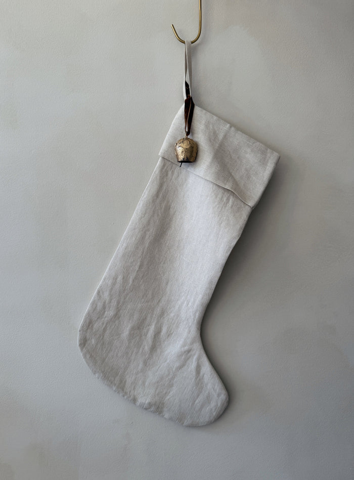 Handmade natural linen Christmas stocking with an antique bell on a white background - Saffron + Poe