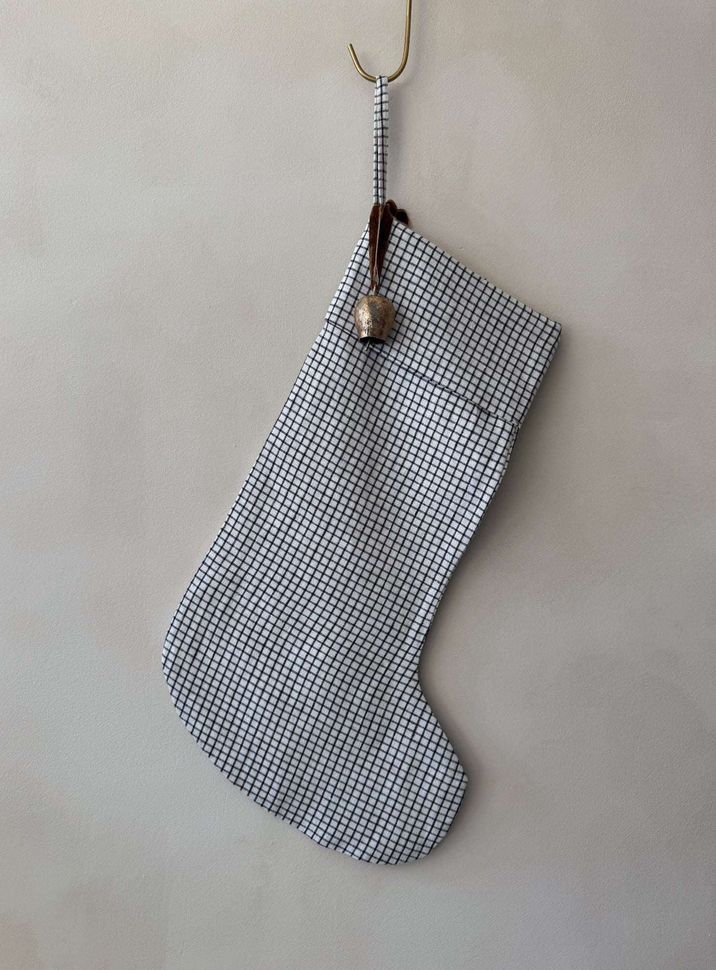 Natural linen stocking with subtle checkered pattern, antique brass bell, and cinnamon ribbon hanging on fireplace mantel