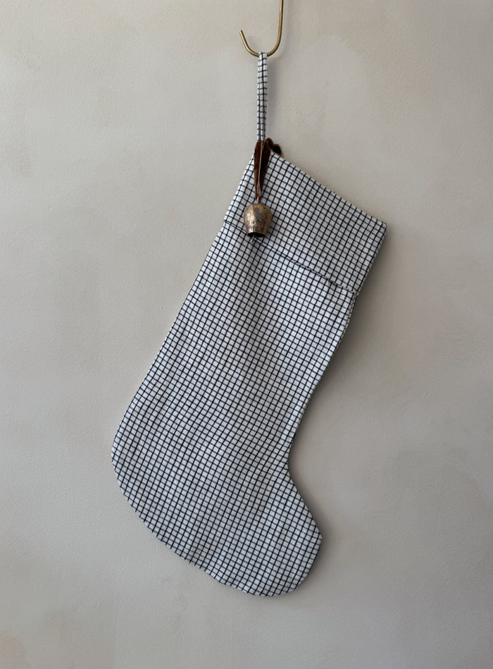 Handmade black and white checkered linen Christmas stocking with an antique bell on a white background - Saffron + Poe