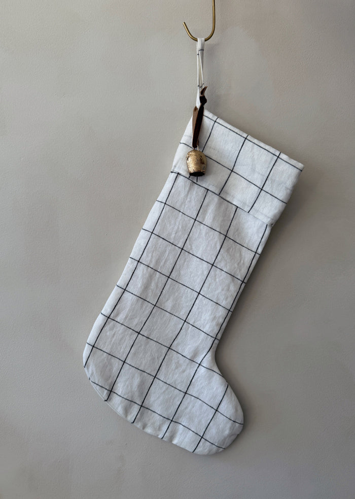 Handmade black and white checkered linen Christmas stocking with an antique bell on a white background - Saffron + Poe