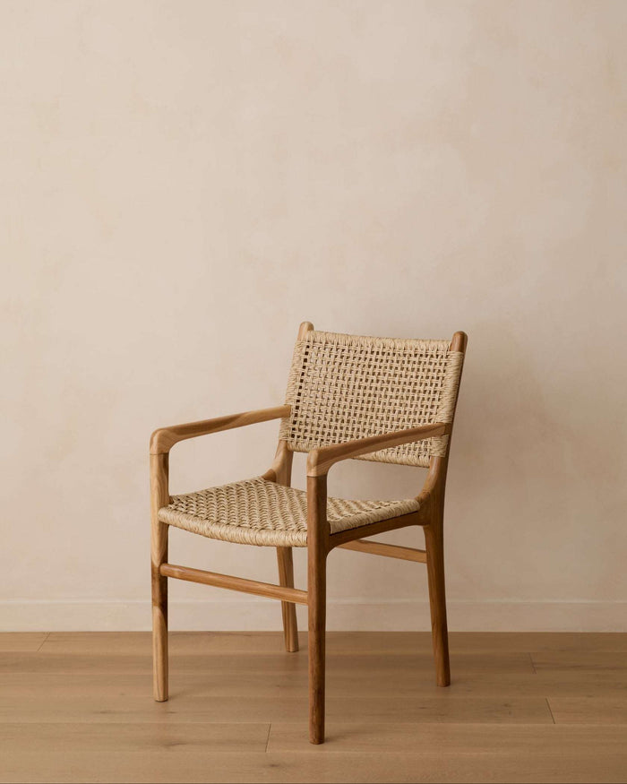 A Marin woven faux rattan dining armchair with a natural wood frame and woven seat and back, set against a minimalist beige wall and light wood floor.