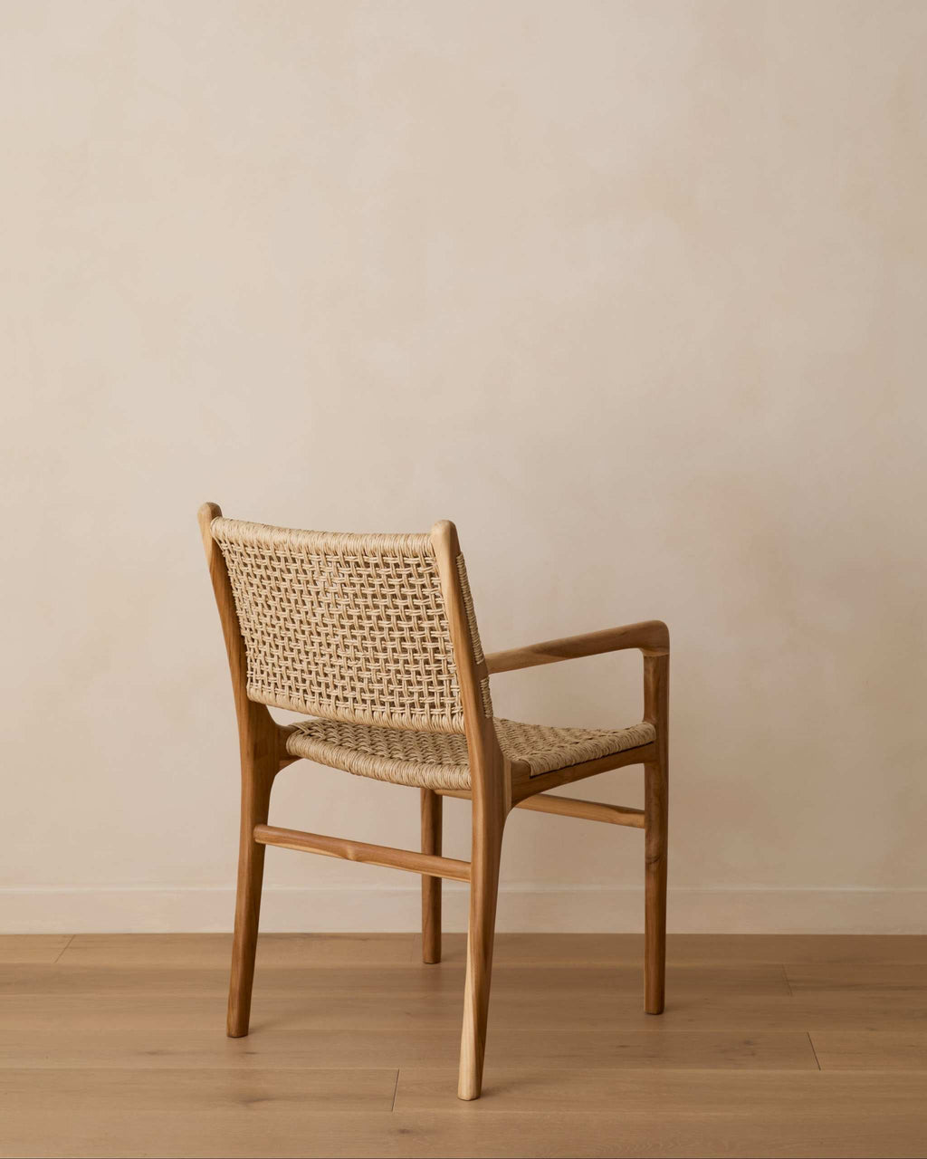 A mid-century modern Marin woven armchair with a woven cane back and seat, positioned against a minimalist beige wall and light wood floor.